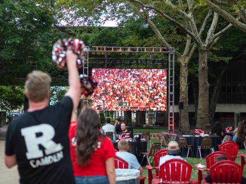 Rutgers–Camden community cheering during football game being shown on big outdoor screen